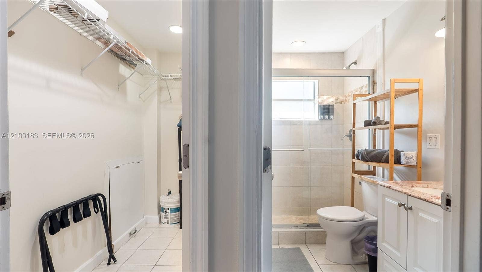 1009 NE 17th Court, Fort Lauderdale, FL 33305 Storage area featuring wire shelving and white tile flooring; bathroom including a vanity with a light-toned stone countertop, a walk-in shower with tiled surround, and recessed lighting