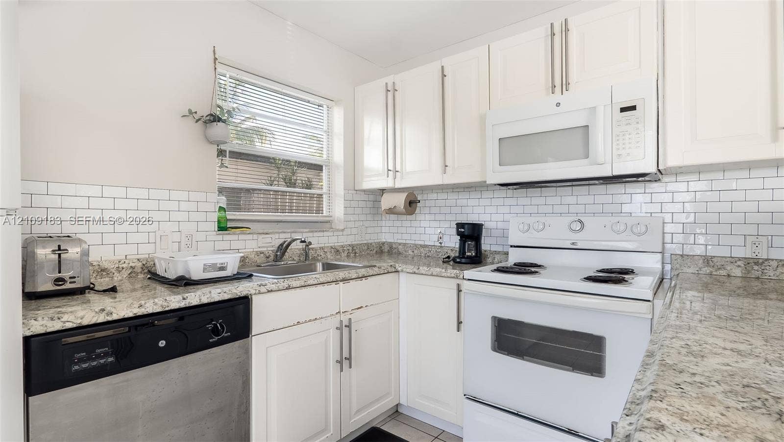1009 NE 17th Court, Fort Lauderdale, FL 33305 Kitchen featuring white cabinetry, stone-finish countertops, subway tile backsplash, and stainless steel and white appliances