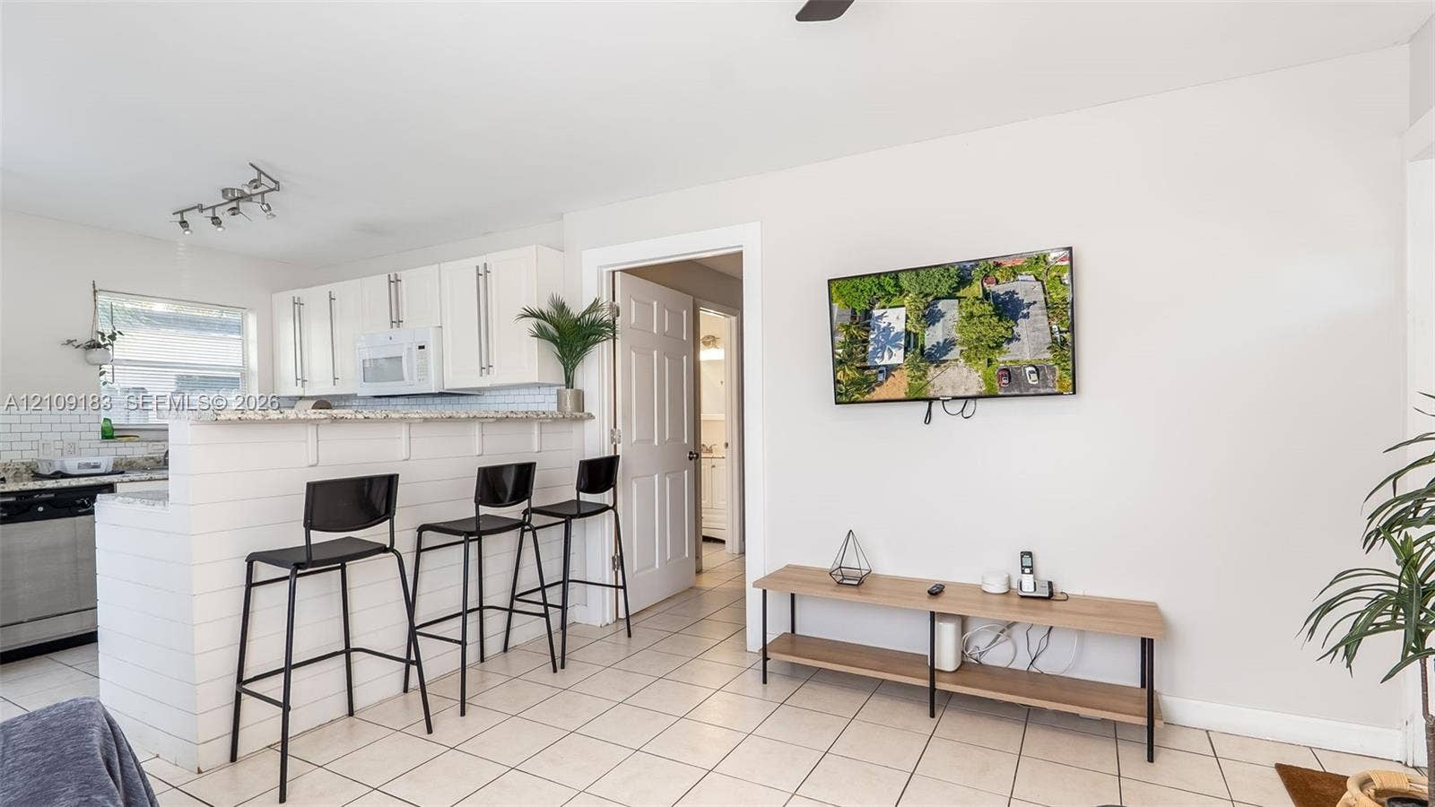 1009 NE 17th Court, Fort Lauderdale, FL 33305 Kitchen featuring white cabinetry, stone-finish countertops, subway tile backsplash, and a breakfast bar with white shiplap detailing, complemented by tile flooring