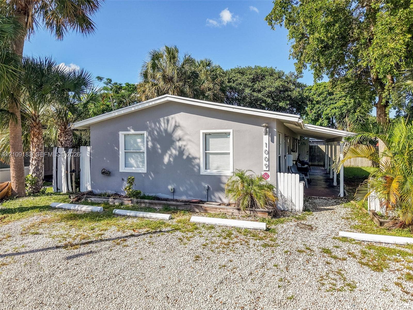 1009 NE 17th Court, Fort Lauderdale, FL 33305 Single-story residence featuring a smooth stucco exterior, dual-pane windows, a covered side porch, and mature palm landscaping
