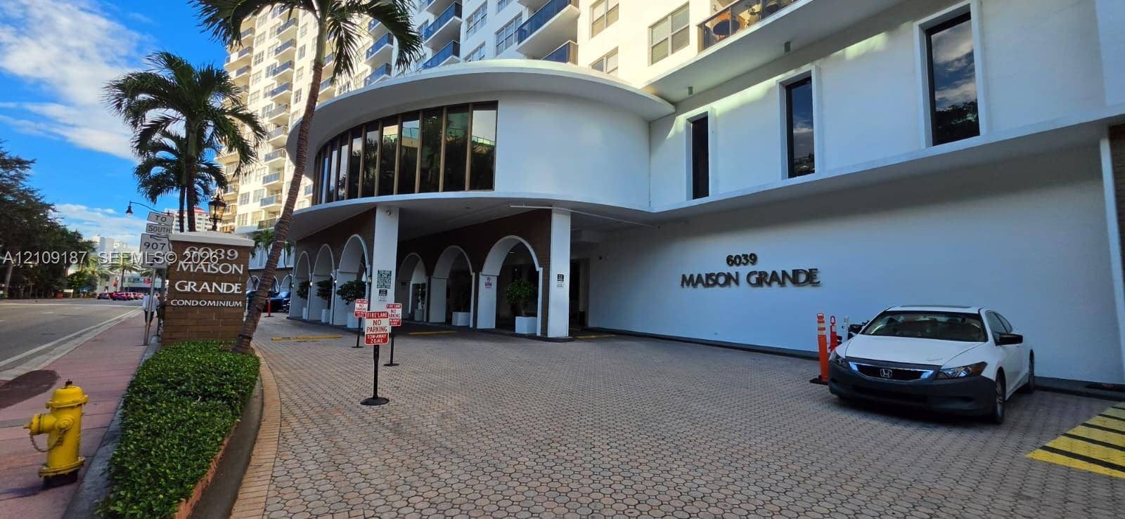 6039 Collins Avenue, #1625, Miami Beach, FL 33140 Exterior facade of the Maison Grande featuring a curved architectural silhouette, covered portico with arched supports, paved motor court, and multi-story balcony configurations