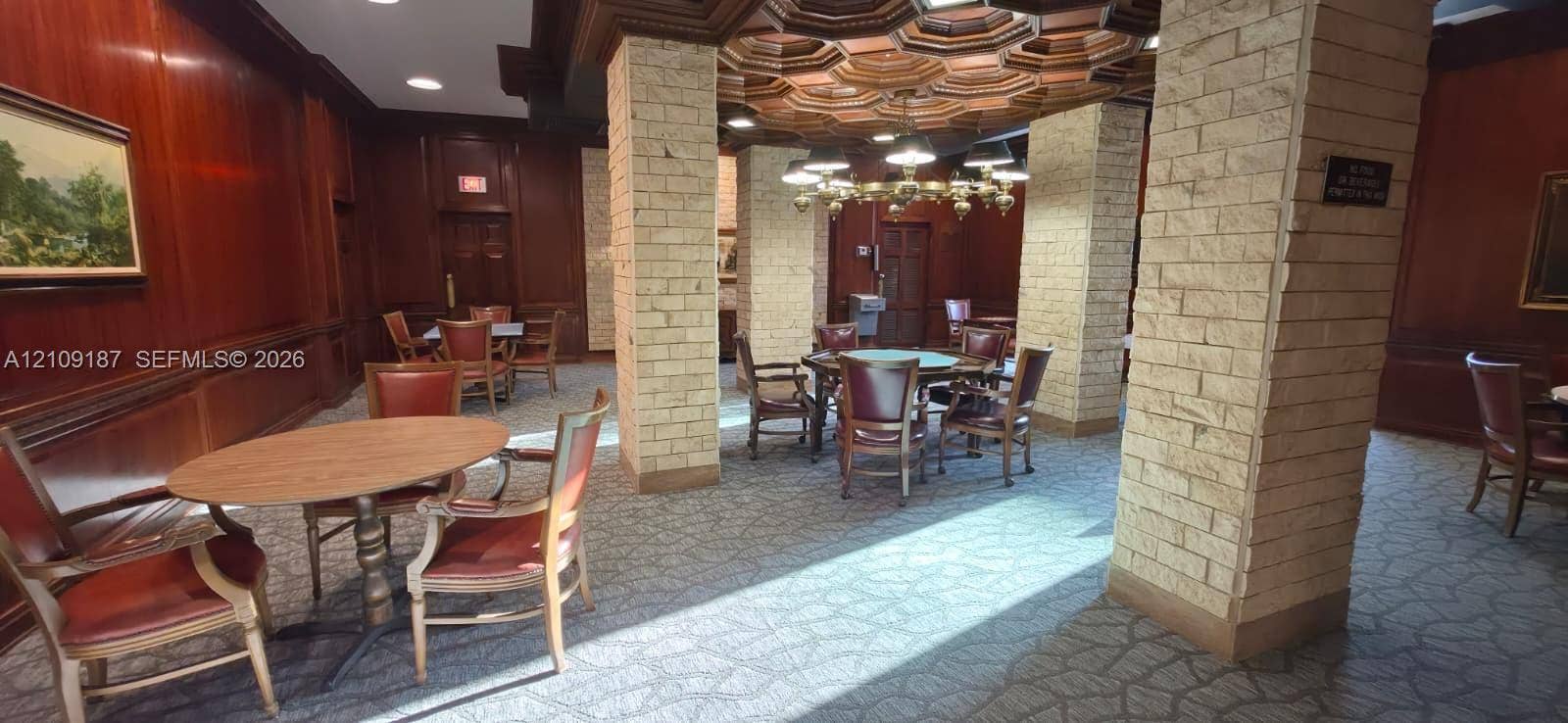 6039 Collins Avenue, #1625, Miami Beach, FL 33140 Men's playroom featuring wood-paneled walls, structural columns finished in textured stone, coffered ceiling, and a multi-tiered metal chandelier