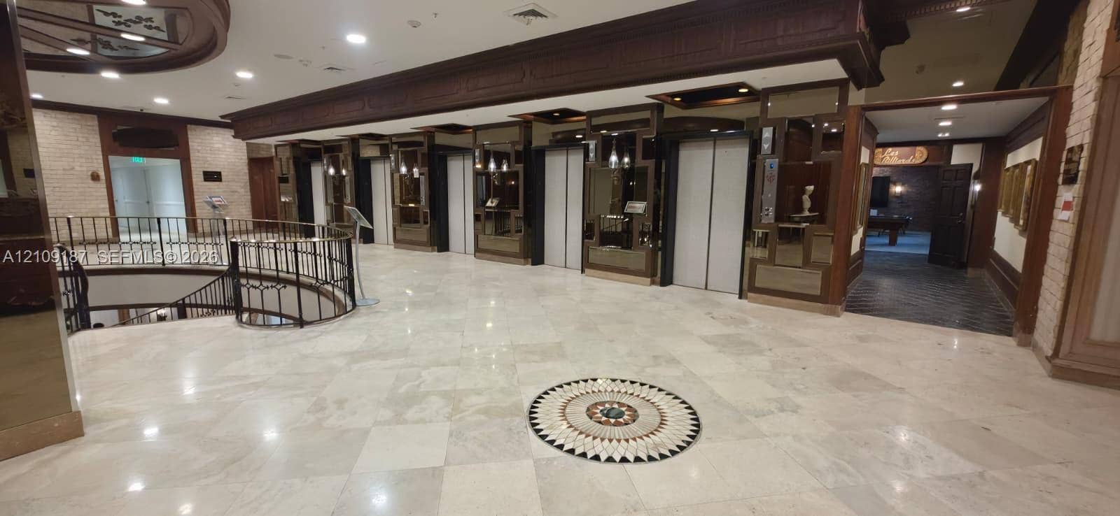 6039 Collins Avenue, #1625, Miami Beach, FL 33140 Grand lobby featuring polished stone tile flooring with decorative inlay, multi-elevator bank, ornate iron stair railing, and wood-paneled accents
