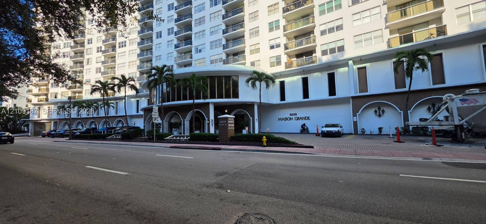 6039 Collins Avenue, #1625, Miami Beach, FL 33140 Mid-rise residential building exterior featuring a porte-cochre entry, arched decorative wall niches, multi-story balconies, and lush palm tree landscaping