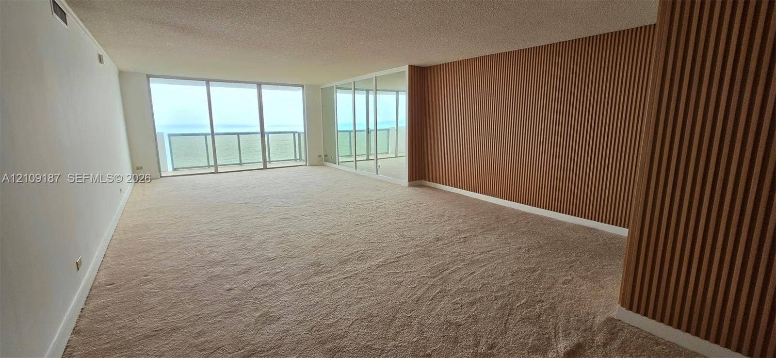 6039 Collins Avenue, #1625, Miami Beach, FL 33140 Spacious dinning-living room featuring floor-to-ceiling mirrored panels and wood-finish wall paneling.