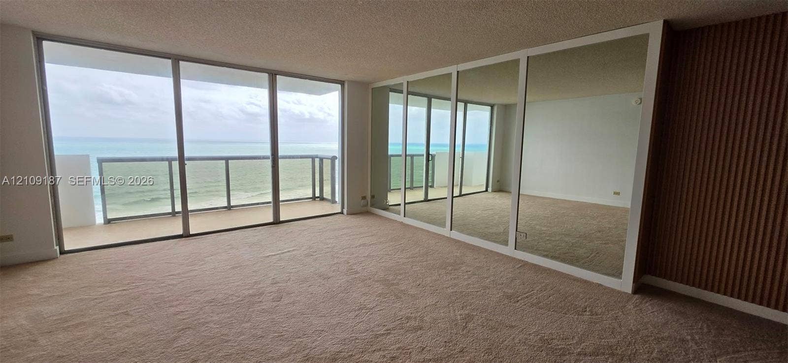6039 Collins Avenue, #1625, Miami Beach, FL 33140 Open-concept space featuring floor-to-ceiling windows, mirrored wall panels to enhance panoramic ocean view, and wood-slat accent wall detailing