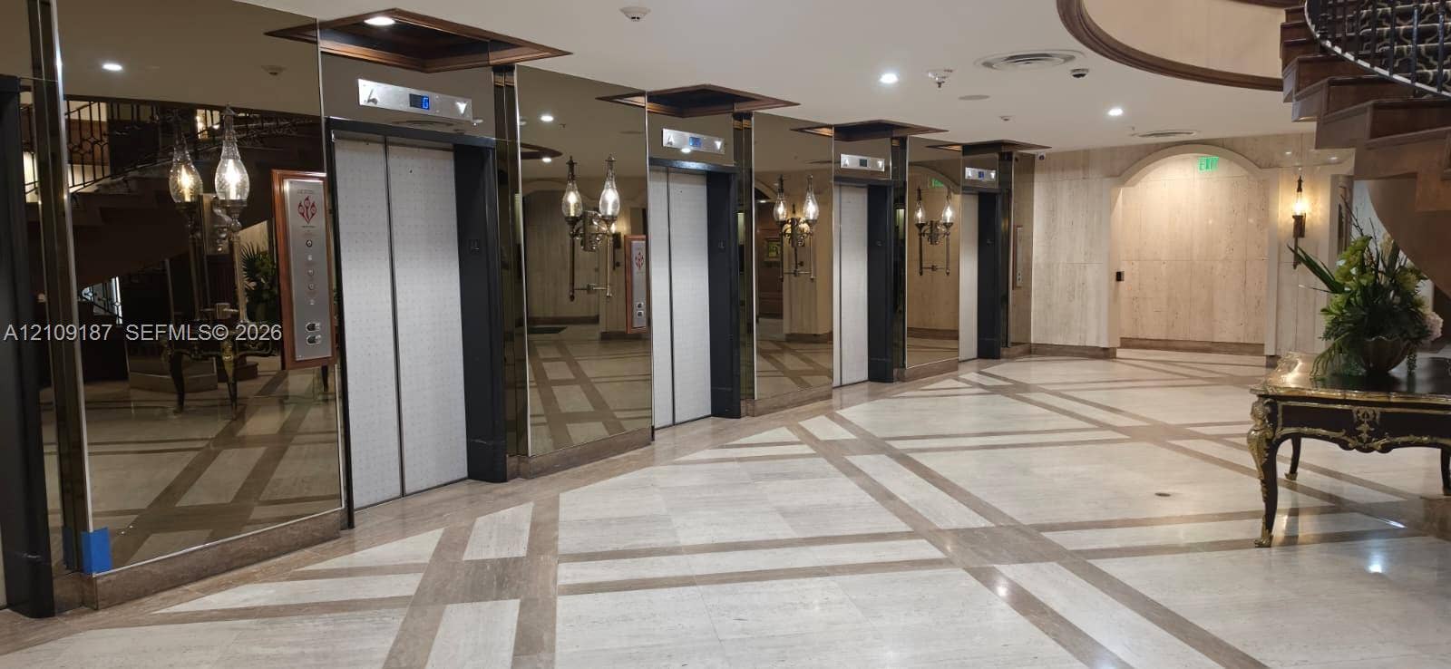 6039 Collins Avenue, #1625, Miami Beach, FL 33140 Grand lobby featuring floor-to-ceiling mirrored walls, a grid-patterned stone floor, a sweeping staircase, and multiple elevator banks