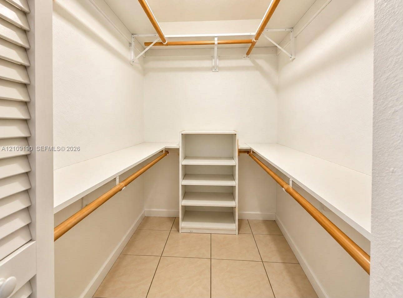 Walk-in closet featuring ceramic tile flooring, built-in shelving unit, and dual-level wooden hanging rods