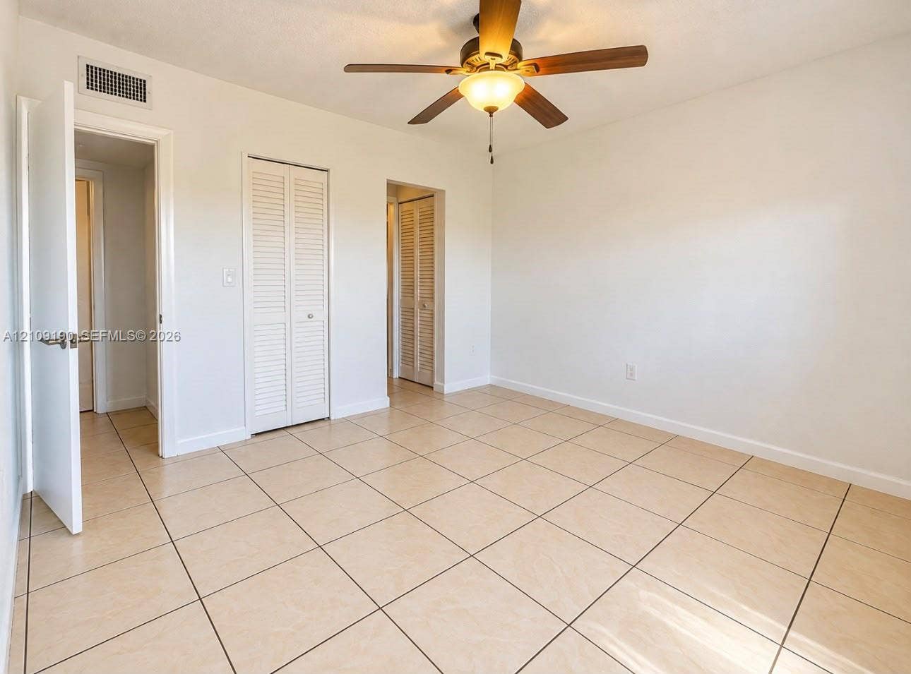 Neutral tile flooring, ceiling fan with integrated lighting, and white louvered-style closet doors