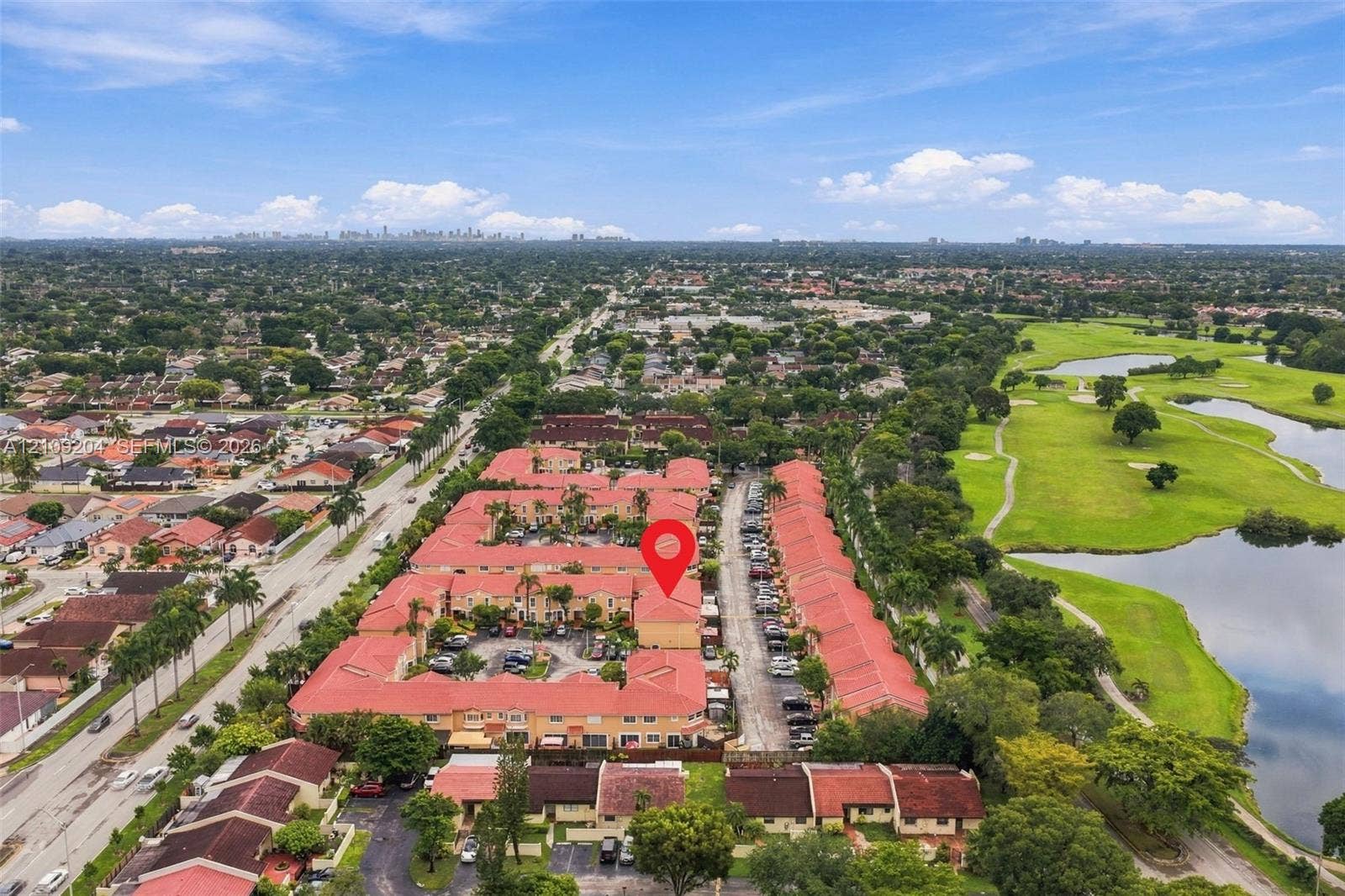 Aerial view of a residential community featuring red tile roofing, paved parking areas, and proximity to expansive golf course grounds with water features