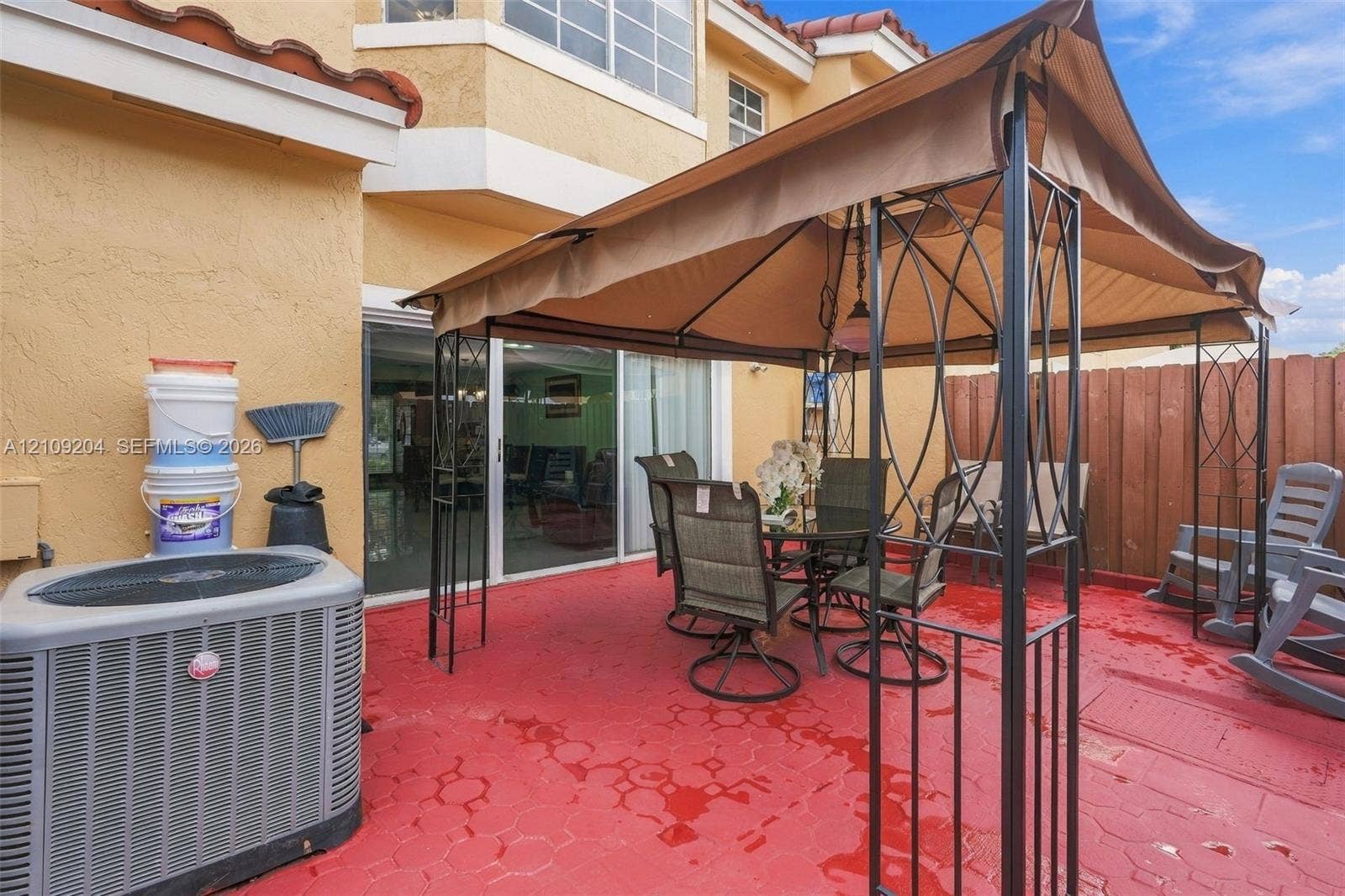Stucco exterior patio featuring a red-toned paver surface, sliding glass entry door, and wood-panel perimeter fencing