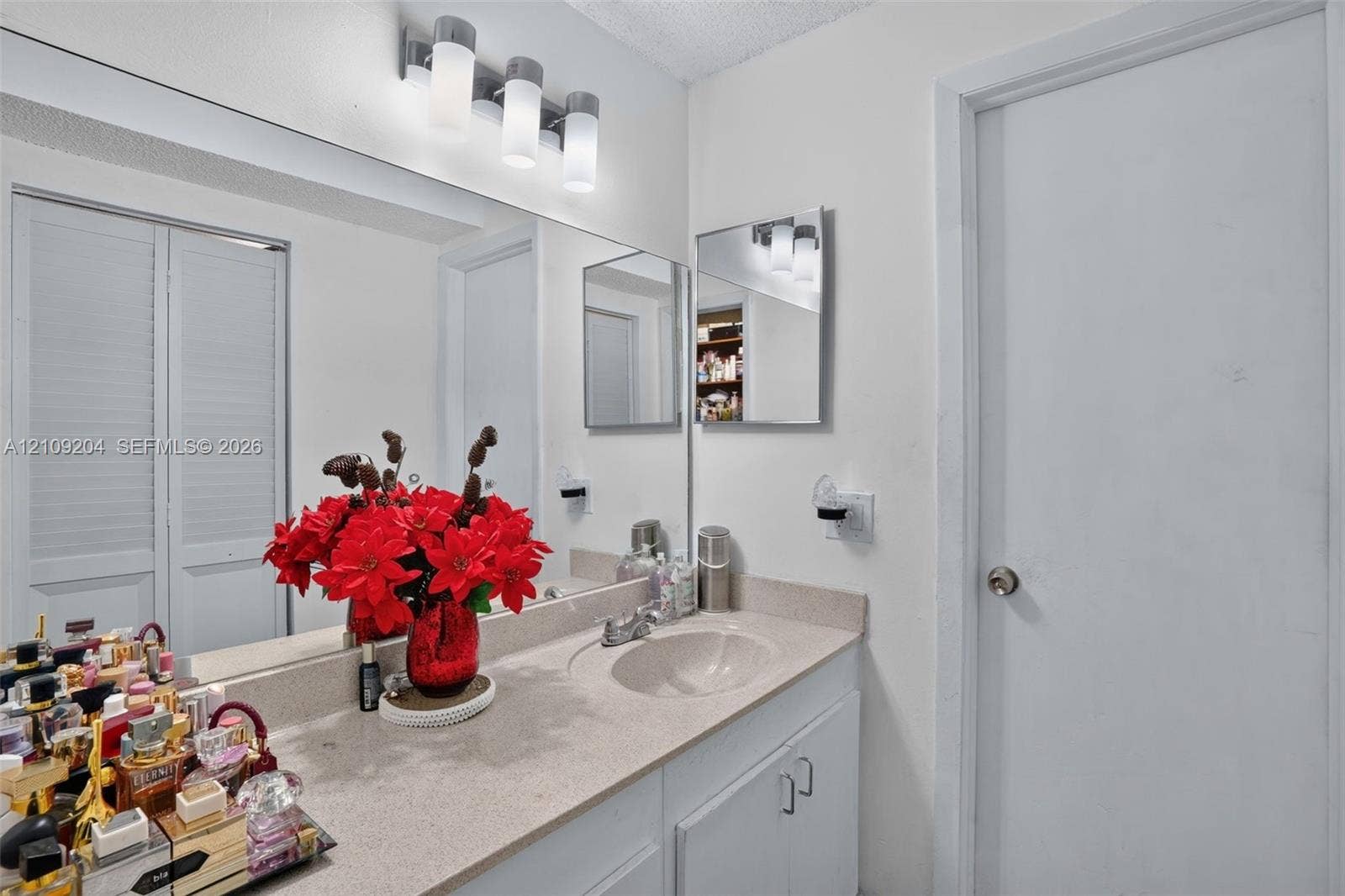 Vanity featuring a stone-composite countertop with an integrated basin, white cabinetry, a large wall-mounted mirror, and a four-light fixture