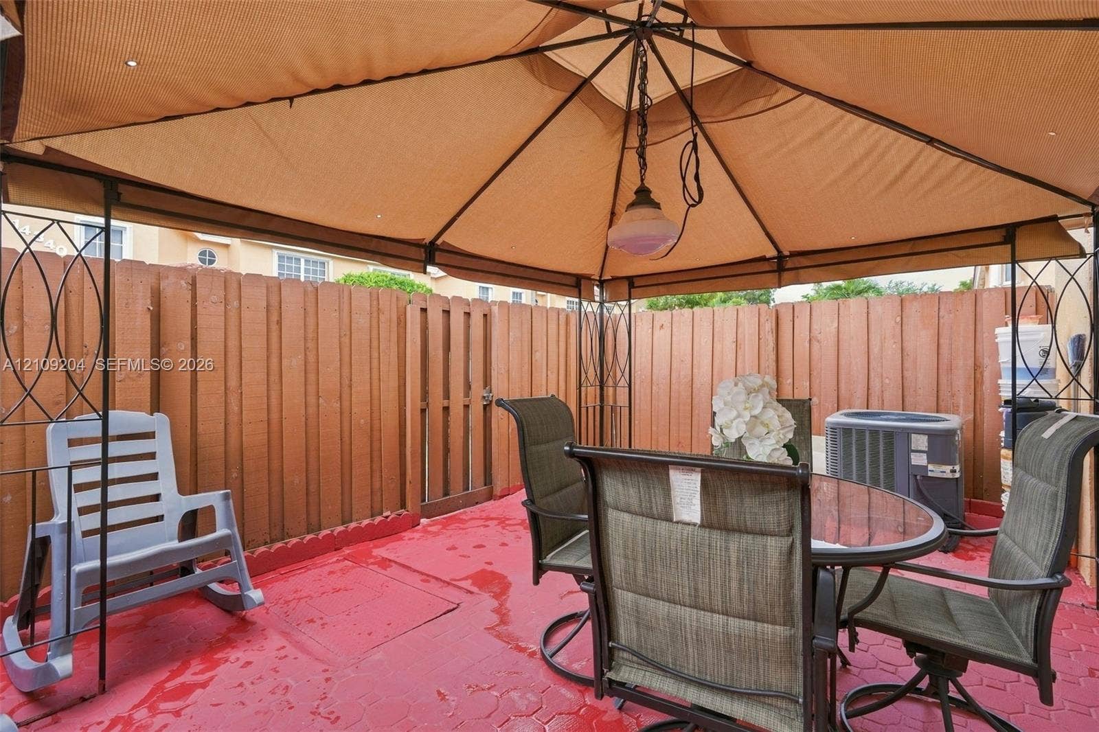 Patio area featuring a metal gazebo structure, stained wood fencing, a locking wooden gate, and painted concrete pavers