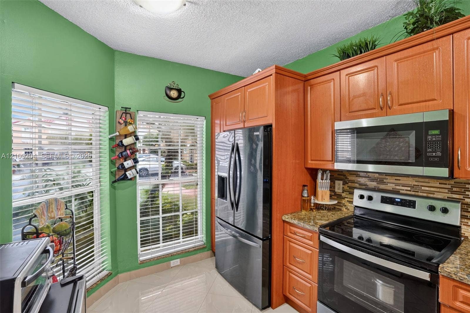 Kitchen featuring wood cabinetry, stone countertops, a mosaic tile backsplash, stainless steel appliances, and dual windows with window blinds