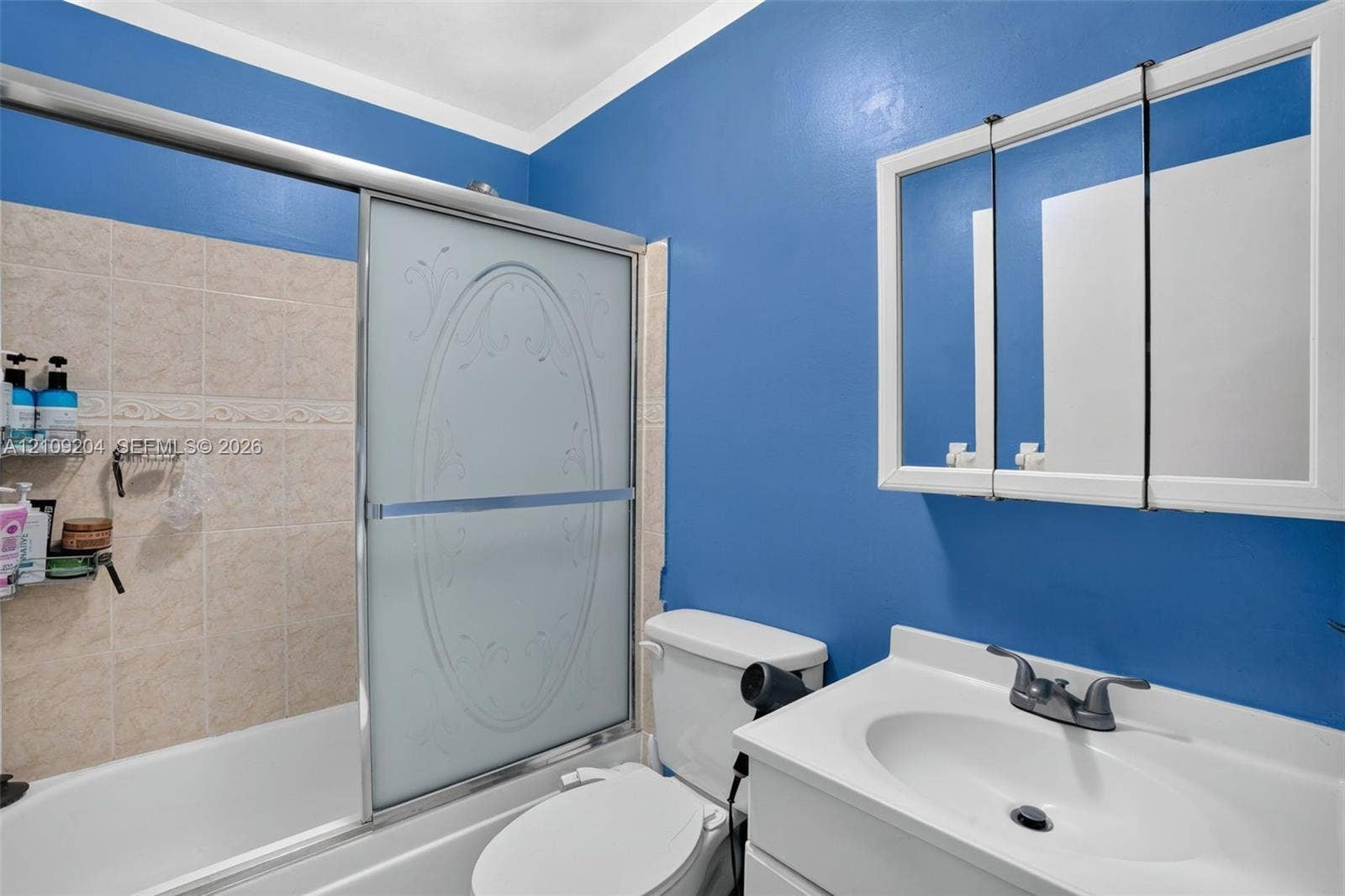 Bathroom featuring a vanity with an integrated basin, a tri-fold medicine cabinet, and a shower-tub combination with sliding glass doors and tiled wall surrounds