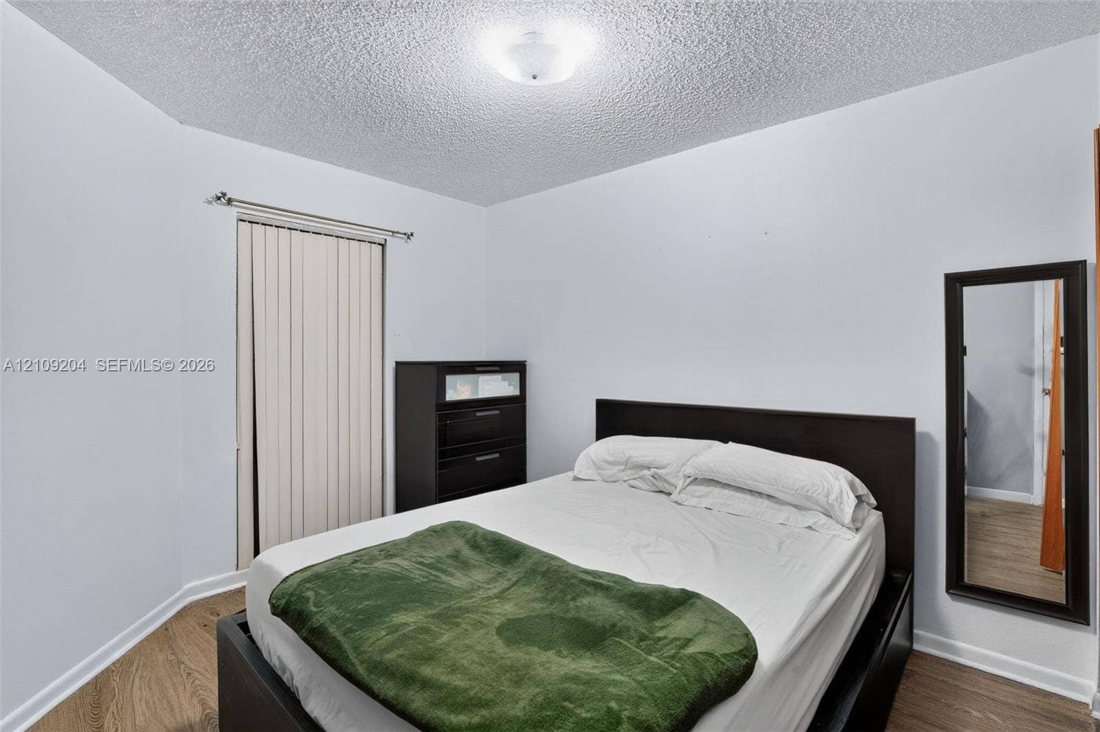 Room featuring wood-finish flooring, textured ceiling, vertical blind window covering, and mounted overhead lighting