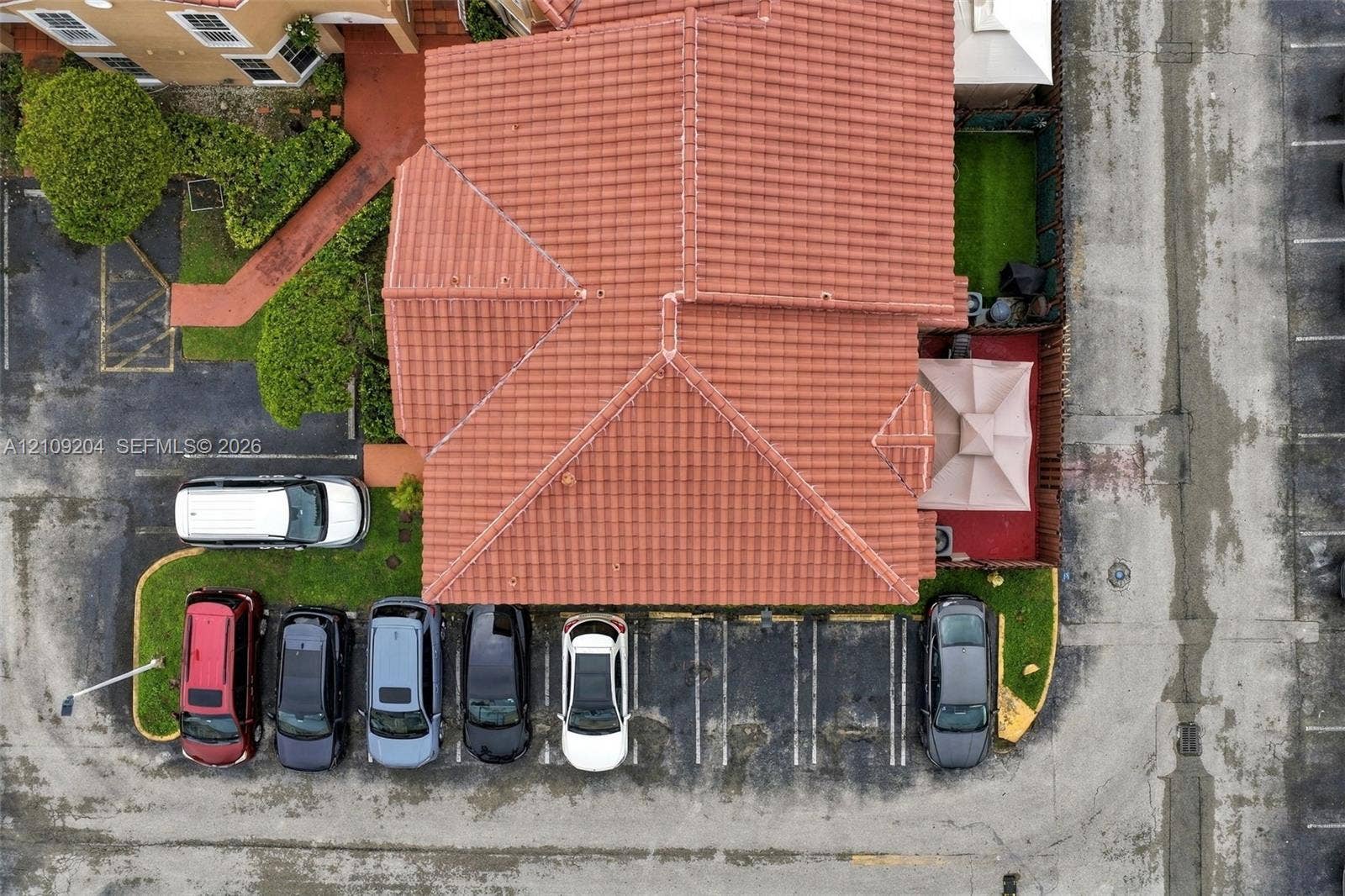Aerial view featuring a terracotta tile roof, designated asphalt parking spaces, and manicured turf landscaping