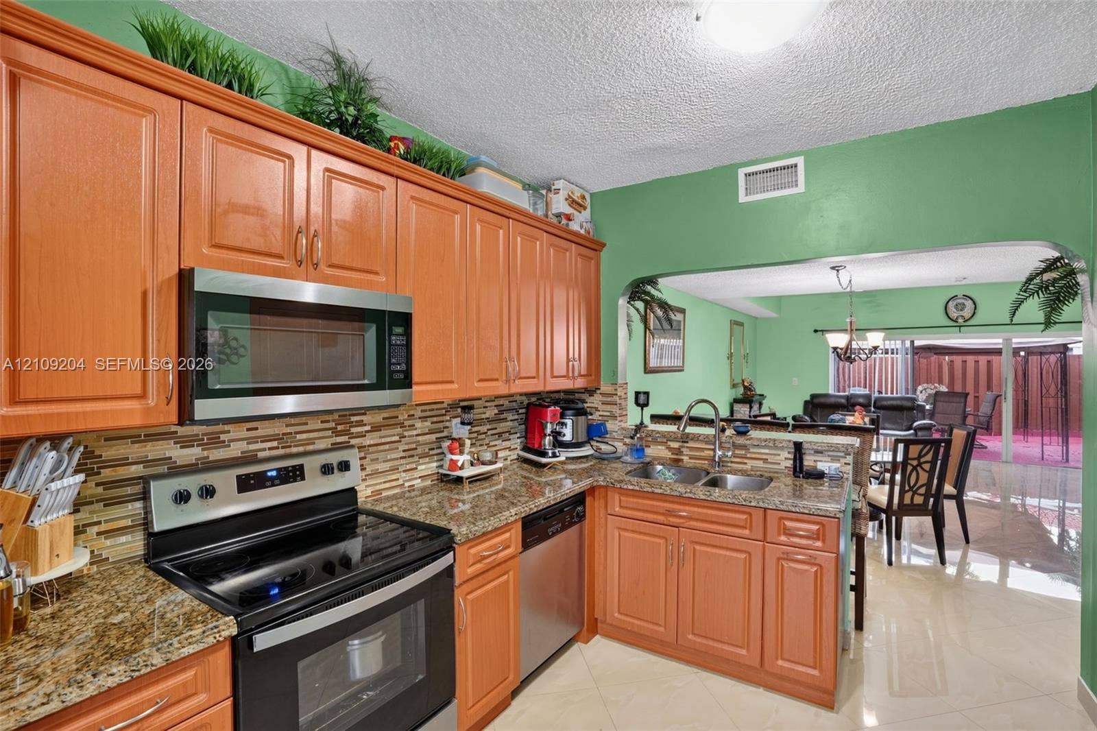 Kitchen featuring raised-panel wood cabinetry, natural stone countertops, a multi-tonal tile backsplash, and stainless steel appliances including a built-in microwave