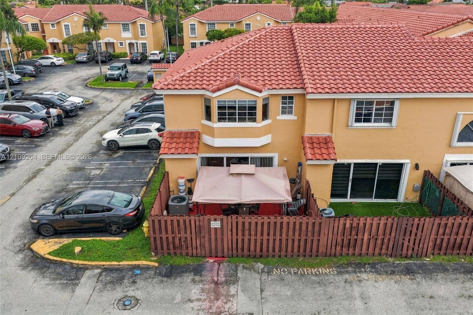 Two-story exterior featuring a clay tile roof, stucco finish, bay window, and a fenced private patio area