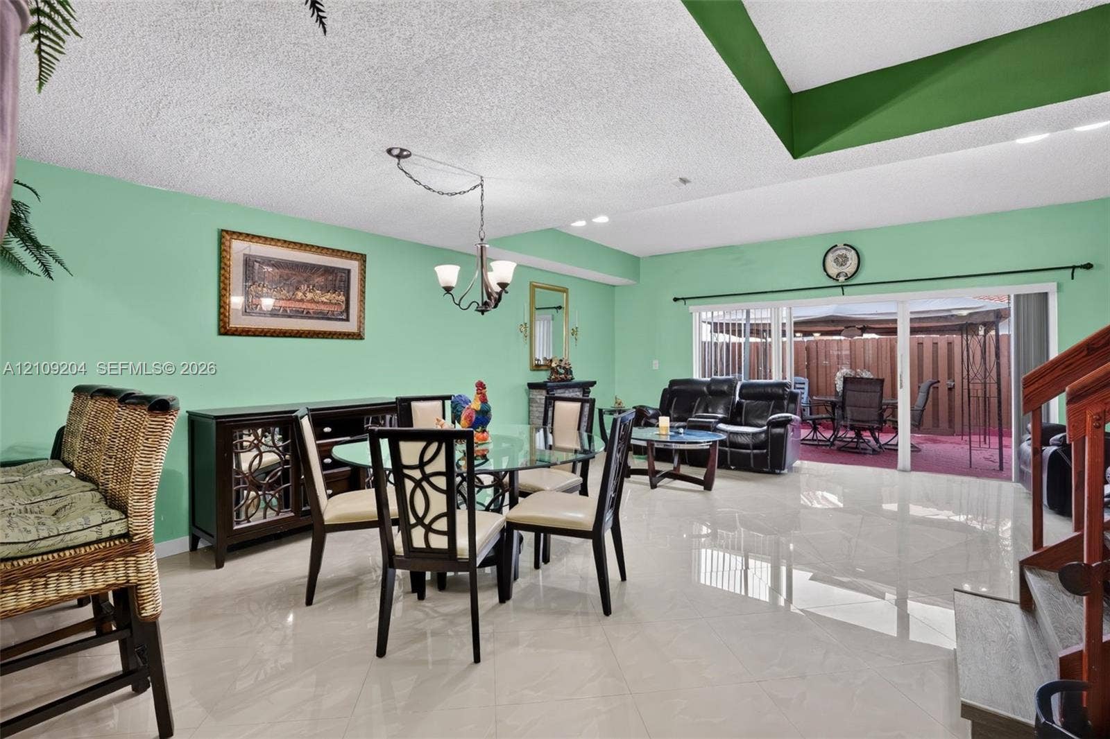 Large-format tile flooring, recessed tray ceiling, sliding glass patio door, and three-arm hanging chandelier