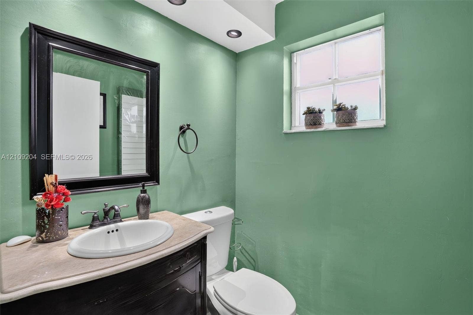Built-in vanity featuring a stone-surface countertop, integrated oval basin, black-framed mirror, and recessed ceiling lighting
