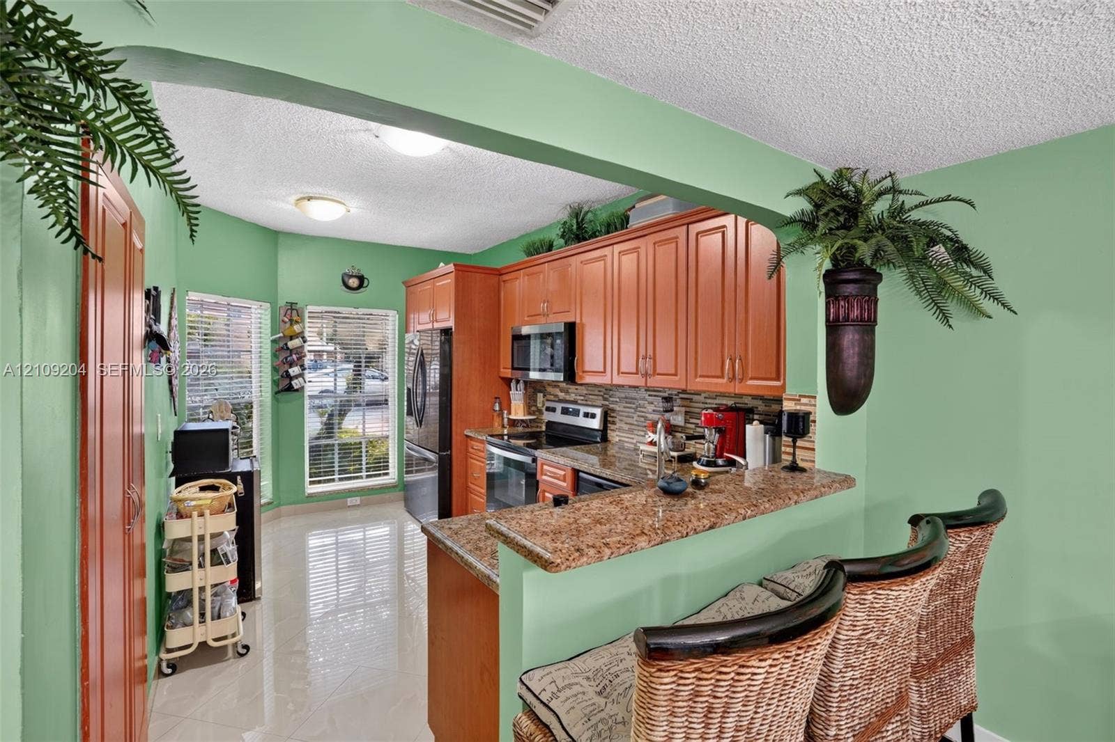 Kitchen featuring wooden cabinetry, stone-surface countertops, stone tile backsplash, integrated stainless steel appliances, and tiled flooring