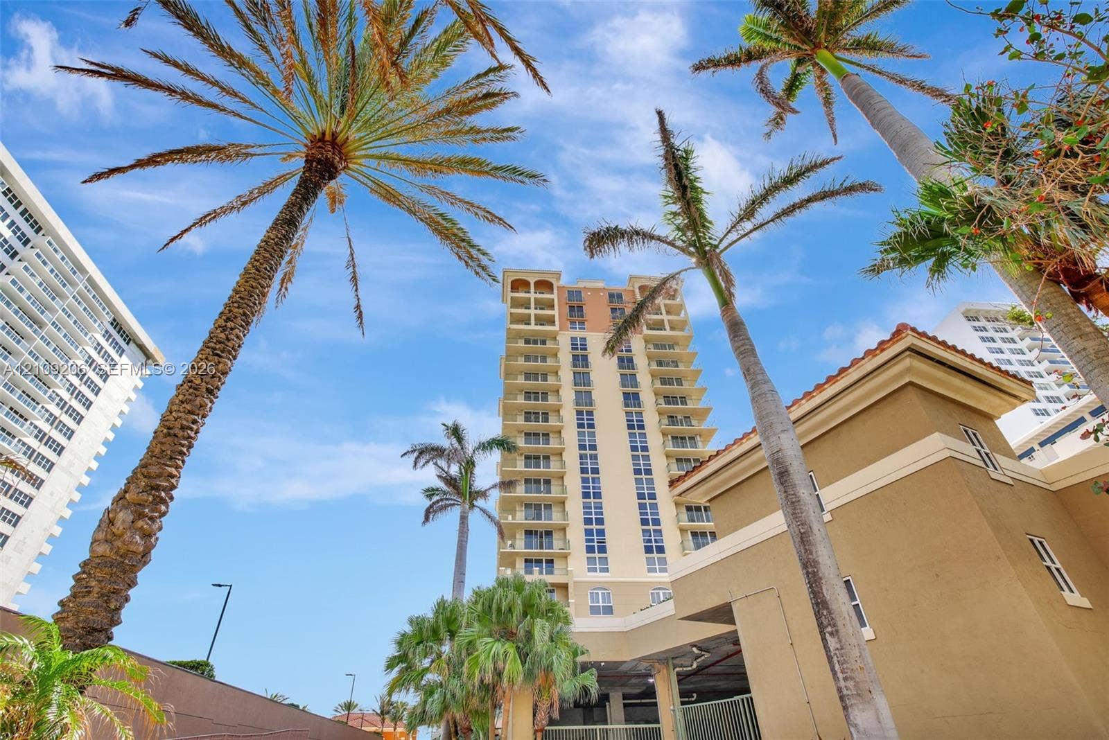 2080 S Ocean Drive, #112, Hallandale Beach, Hallandale Beach, FL 33009 Multi-story residential building exterior featuring a stucco facade, rows of private recessed balconies, and mature palm trees