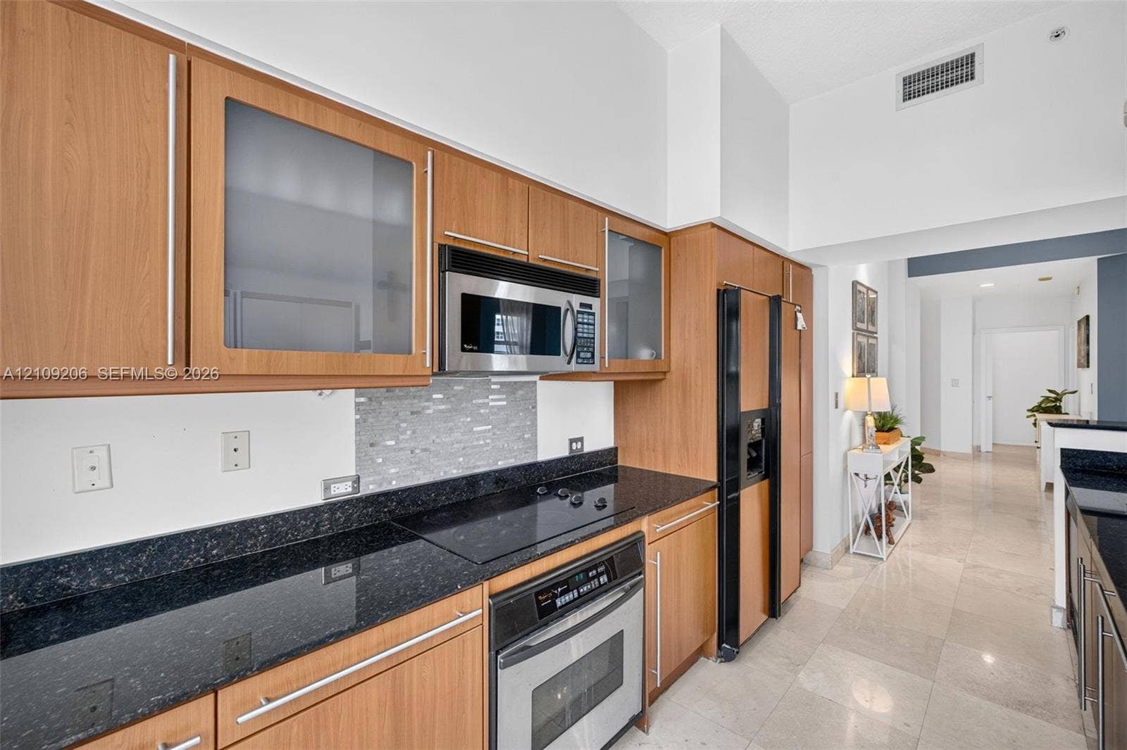 2080 S Ocean Drive, #112, Hallandale Beach, Hallandale Beach, FL 33009 Kitchen featuring wood-finish cabinetry with frosted glass inserts, dark stone-finish countertops, tile backsplash, built-in stainless steel appliances, and tile flooring