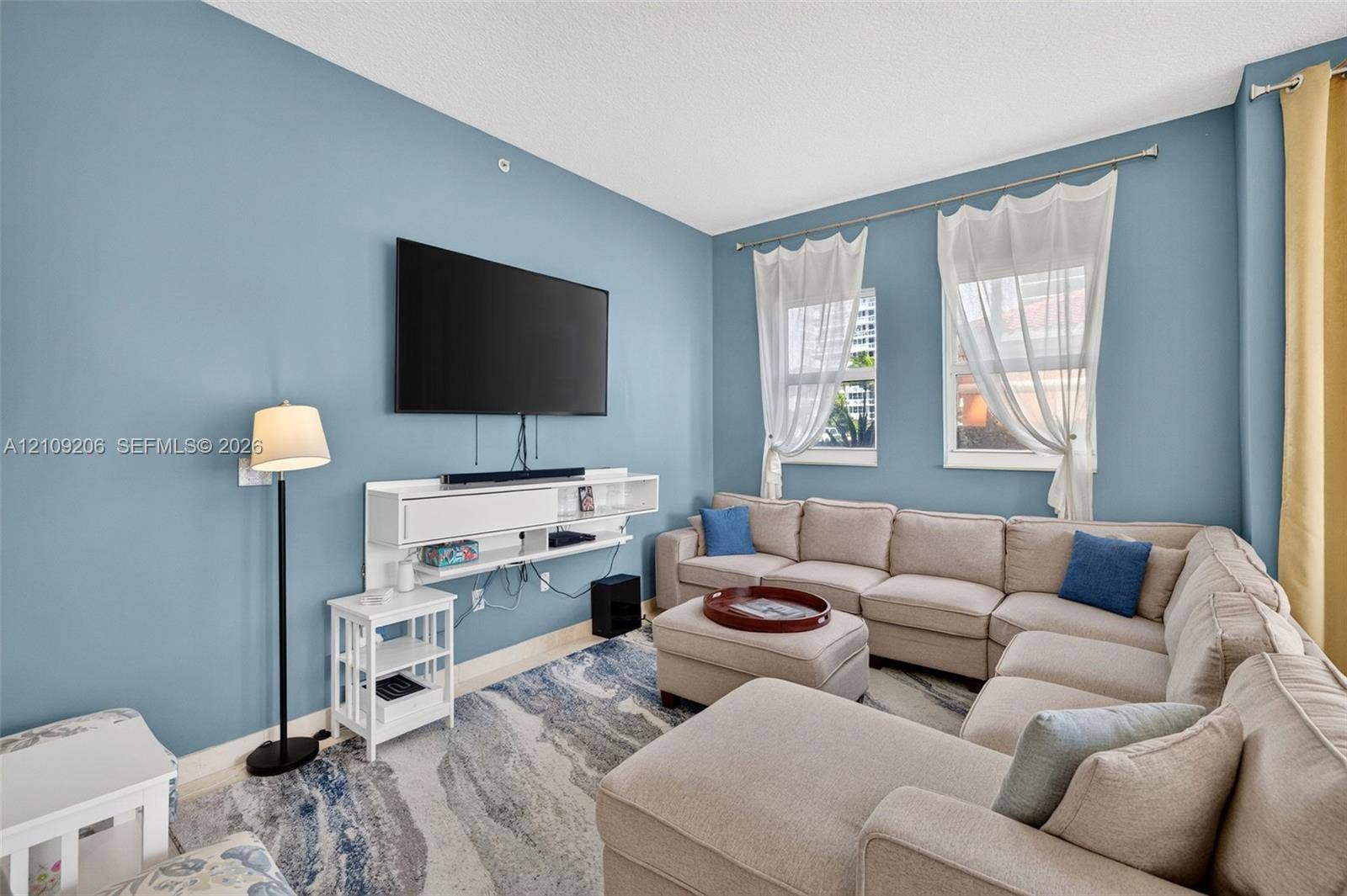 2080 S Ocean Drive, #112, Hallandale Beach, Hallandale Beach, FL 33009 Living area featuring a wall-mounted white media console and two windows with hardware-mounted curtain rods