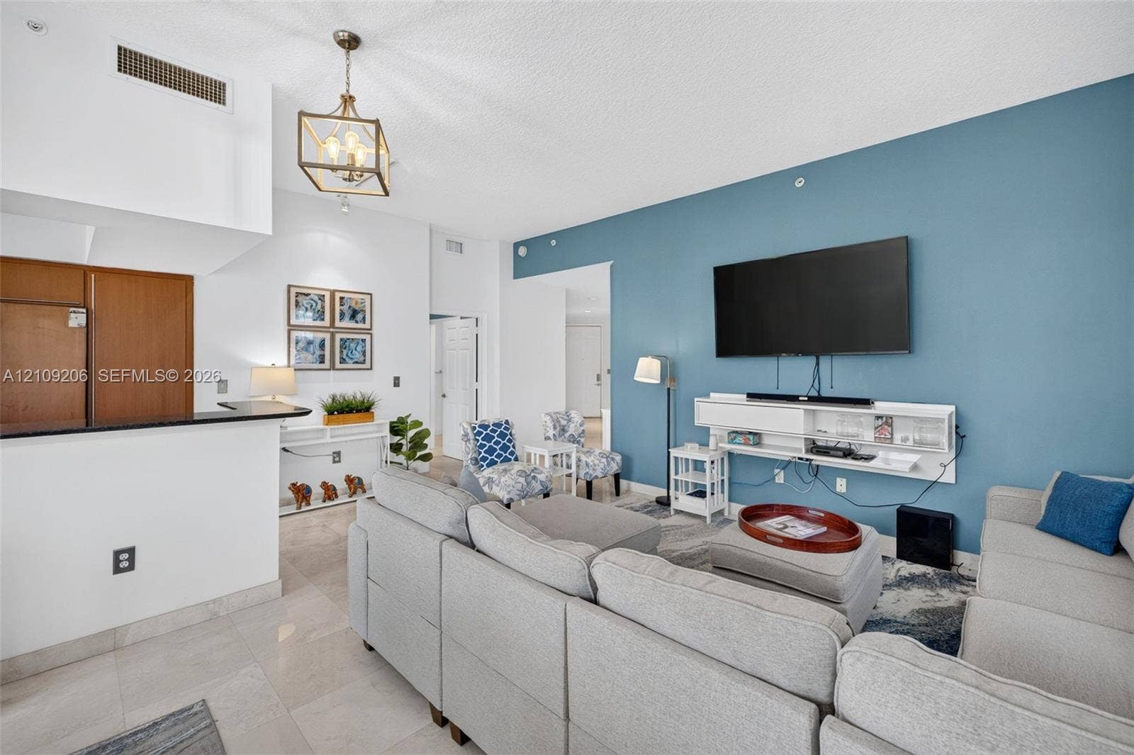 2080 S Ocean Drive, #112, Hallandale Beach, Hallandale Beach, FL 33009 Living area featuring a high ceiling, metallic geometric pendant lighting, stone-finish tile flooring, a dual-tone accent wall, and a custom built-in white wall-mounted media console