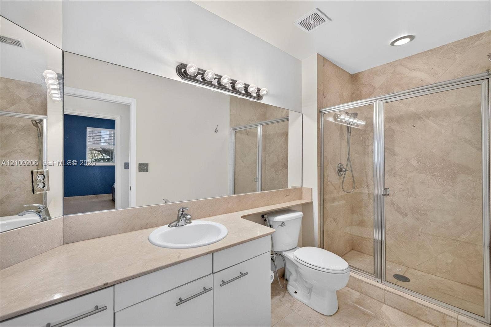 2080 S Ocean Drive, #112, Hallandale Beach, Hallandale Beach, FL 33009 Full-width wall mirror above a vanity with stone-surfaced countertop, integrated sink, metal-finish hardware, and a walk-in shower enclosure featuring tiled walls