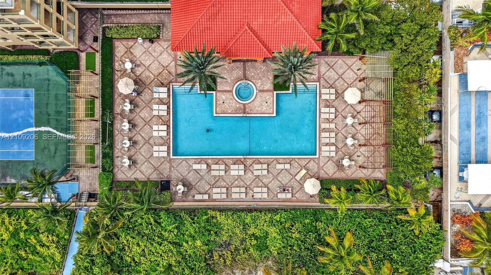 2080 S Ocean Drive, #112, Hallandale Beach, Hallandale Beach, FL 33009 Aerial perspective of a multi-feature recreation area including a large swimming pool, an integrated spa, a tennis court with perimeter fencing, and expansive paver decking surrounded by mature trees and landscaped hedges