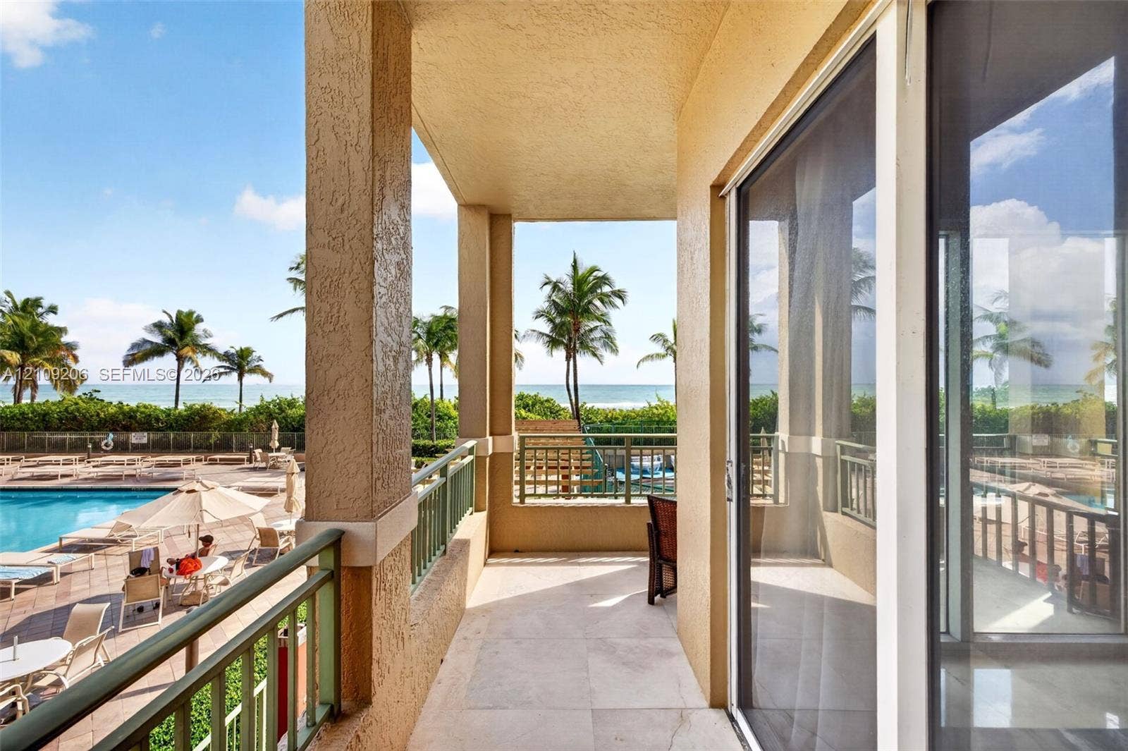 2080 S Ocean Drive, #112, Hallandale Beach, Hallandale Beach, FL 33009 Covered balcony featuring stone flooring and metal railings, overlooking an outdoor swimming pool and coastal scenery