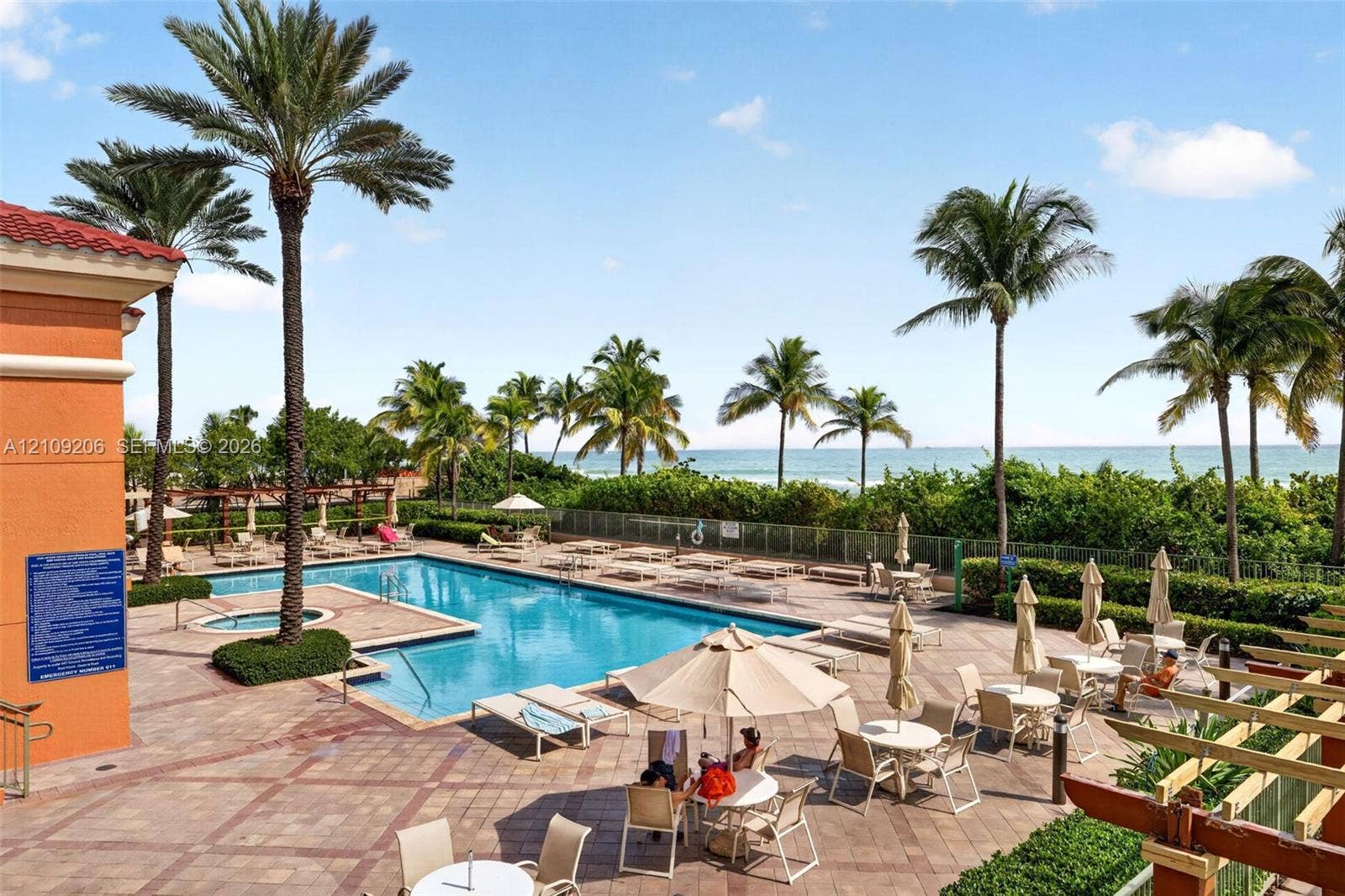 2080 S Ocean Drive, #112, Hallandale Beach, Hallandale Beach, FL 33009 Swimming pool and integrated spa featuring a patterned paver deck, perimeter palm trees, and coastal water backdrop