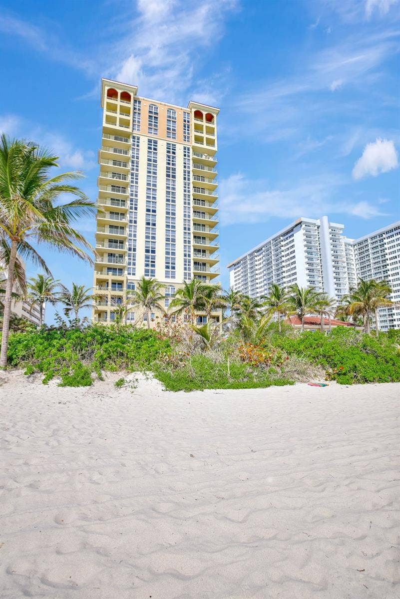 2080 S Ocean Drive, #112, Hallandale Beach, Hallandale Beach, FL 33009 High-rise structure featuring stacked balconies, exterior arch details, sand-covered beach, and lush palm-lined vegetation