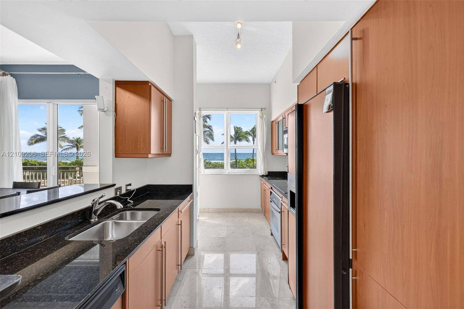 2080 S Ocean Drive, #112, Hallandale Beach, Hallandale Beach, FL 33009 Kitchen featuring custom wood cabinetry, dark stone countertops, stainless steel double-basin sink, stone flooring, and windows with ocean scenery