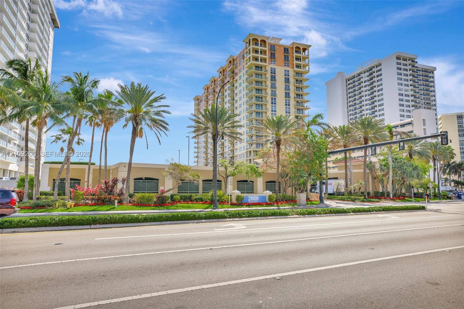 2080 S Ocean Drive, #112, Hallandale Beach, Hallandale Beach, FL 33009 High-rise building exterior featuring architectural balconies, stucco facade, mature palm trees, manicured landscaping, and structured green space