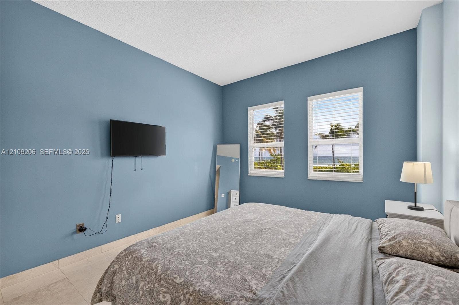 2080 S Ocean Drive, #112, Hallandale Beach, Hallandale Beach, FL 33009 Spacious bedroom featuring light-toned tile flooring, two windows with horizontal blinds, and a coastal landscape visible through the glass