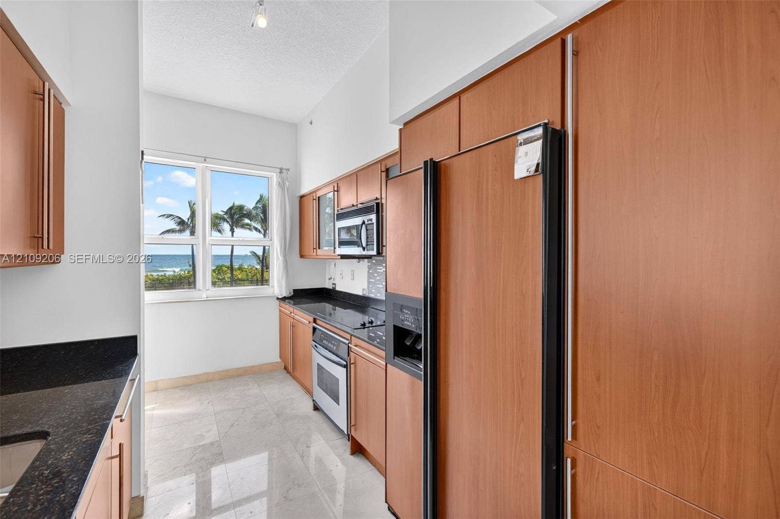 2080 S Ocean Drive, #112, Hallandale Beach, Hallandale Beach, FL 33009 Kitchen featuring wood-veneer cabinetry, dark stone countertops, tile flooring, and stainless steel appliances with an ocean horizon backdrop