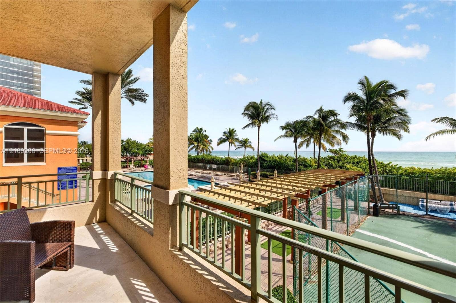 2080 S Ocean Drive, #112, Hallandale Beach, Hallandale Beach, FL 33009 Covered balcony featuring metal railings, overlooking a tennis court, a wooden pergola, a swimming pool, and the ocean