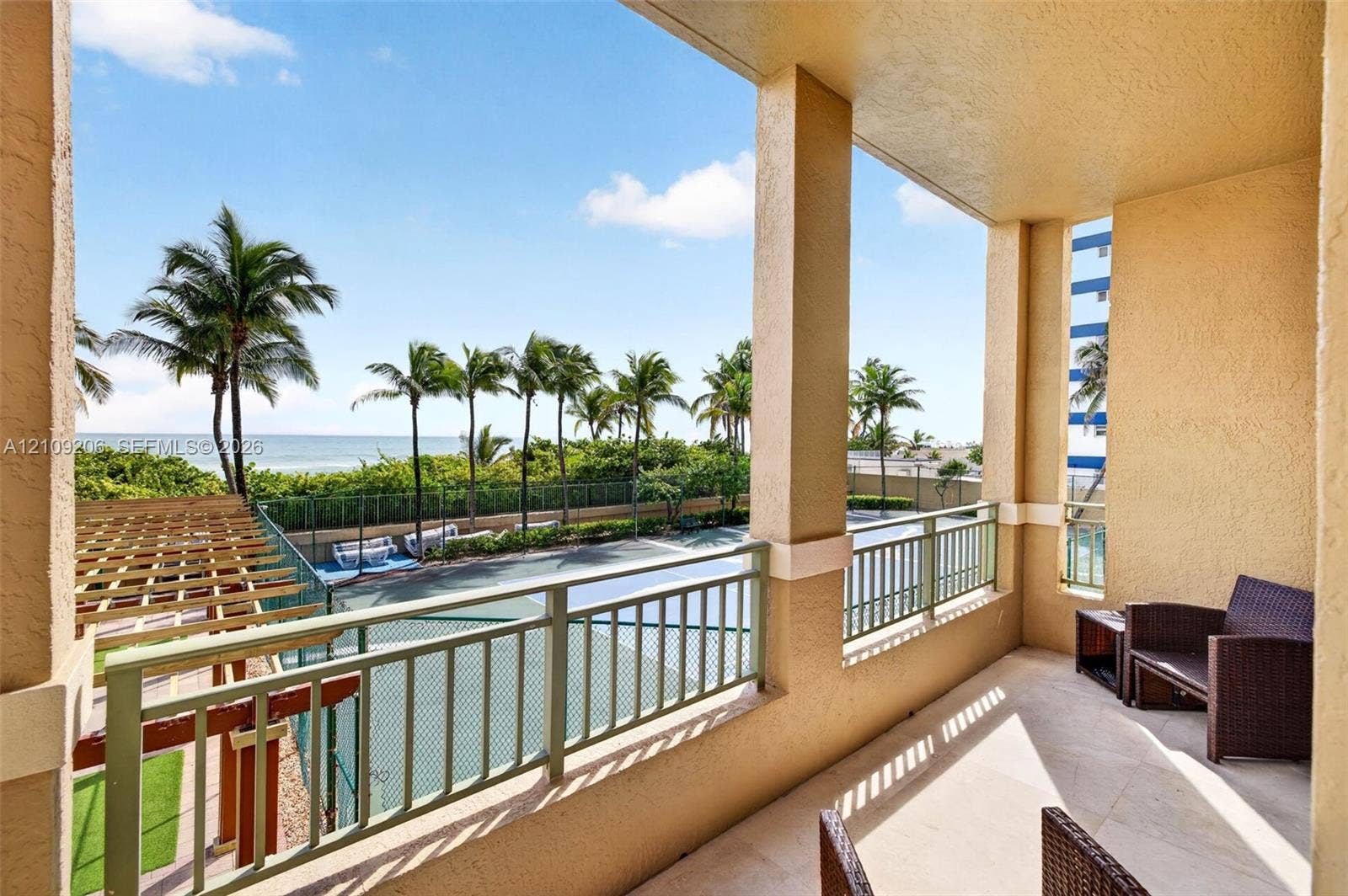 2080 S Ocean Drive, #112, Hallandale Beach, Hallandale Beach, FL 33009 Covered balcony featuring stone-finish flooring, metal railing, and structural pillars, overlooking a hard-surface court and tropical landscaping