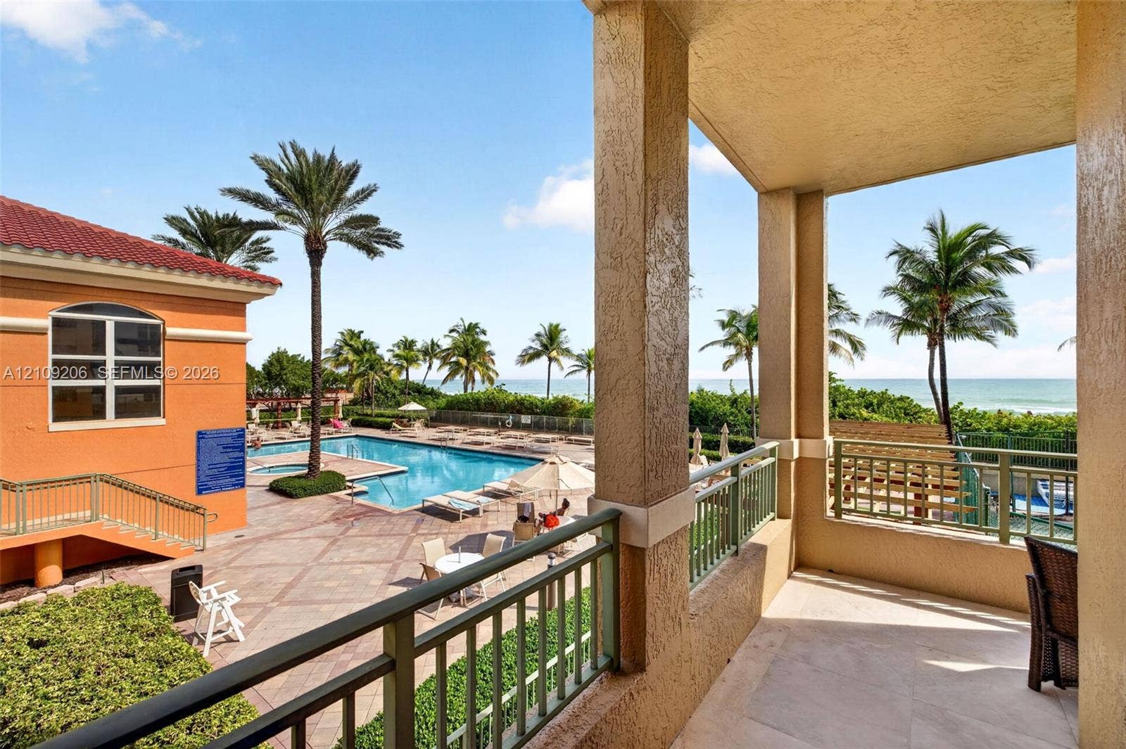 2080 S Ocean Drive, #112, Hallandale Beach, Hallandale Beach, FL 33009 Covered balcony with stone flooring, metal railings, and stucco columns overlooking a swimming pool, palm trees, and ocean horizon