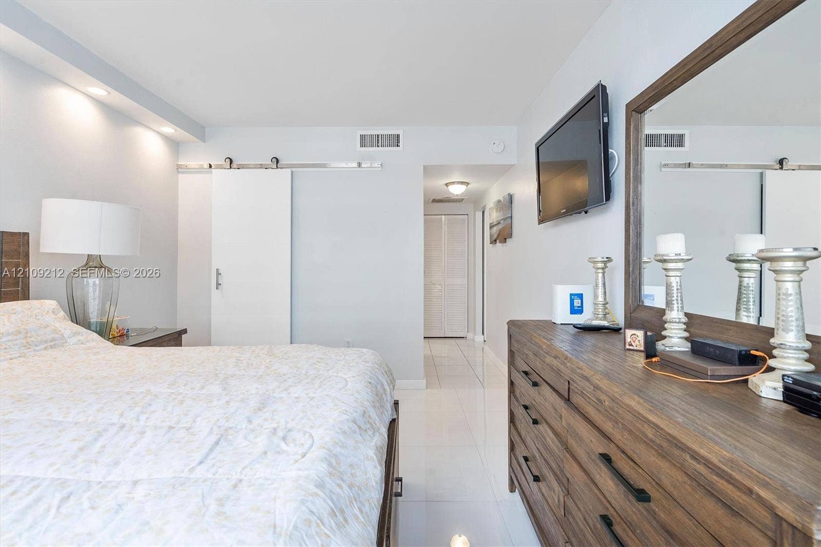 Polished tile flooring, sliding barn door with metallic hardware, recessed ceiling lighting, and double-door closet cabinetry