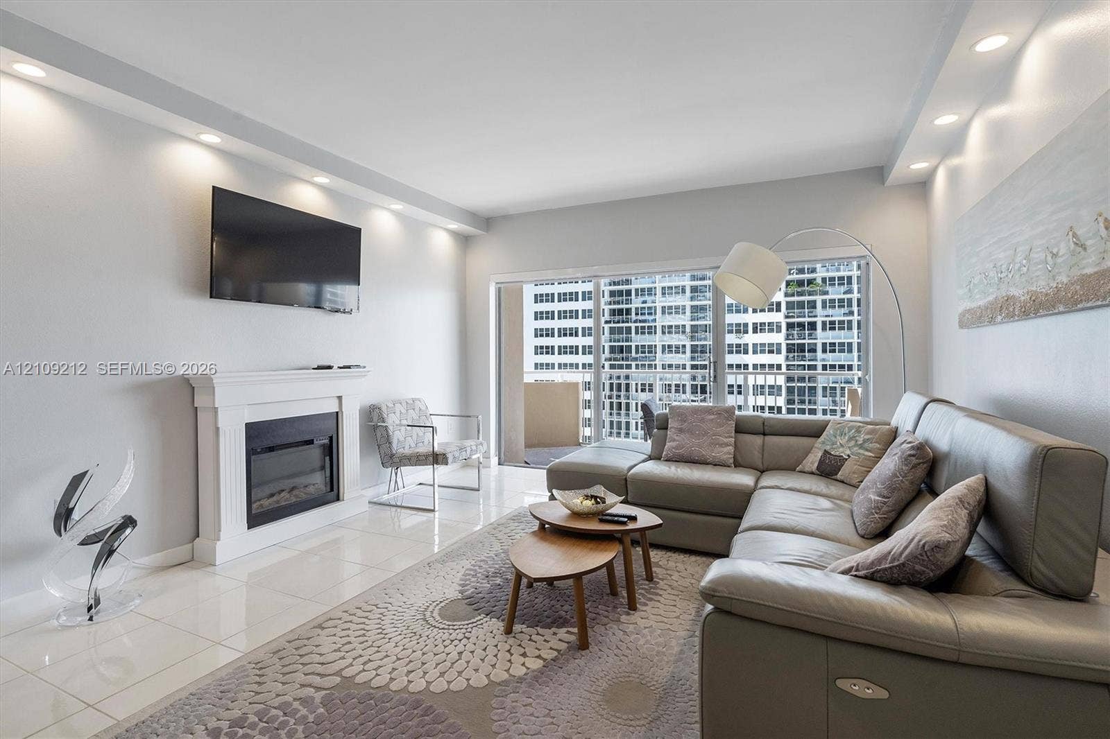 Living area featuring a white fireplace mantel, polished tile flooring, recessed ceiling lighting, and sliding glass doors leading to a balcony