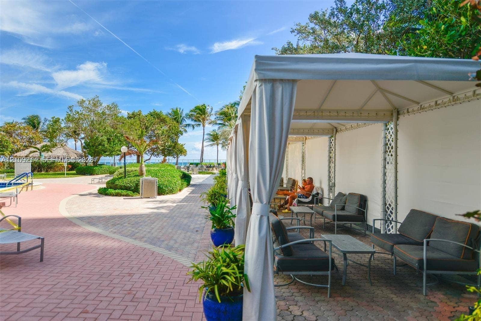 Outdoor patio featuring brick paver hardscaping, a large permanent fabric canopy structure, and mature landscaping