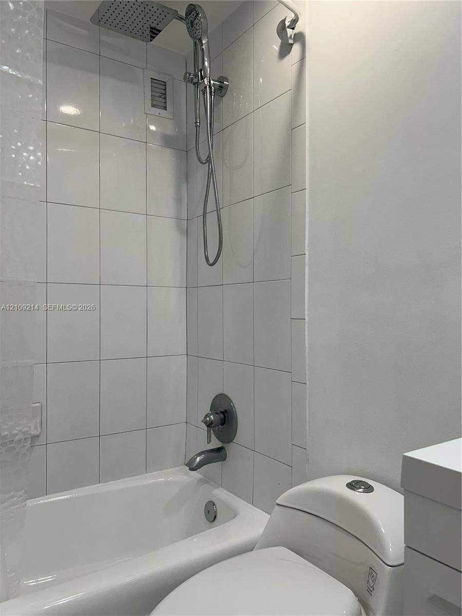 Shower and tub combination featuring white wall tiling, a rainfall showerhead, and a handheld shower attachment with metallic fixtures