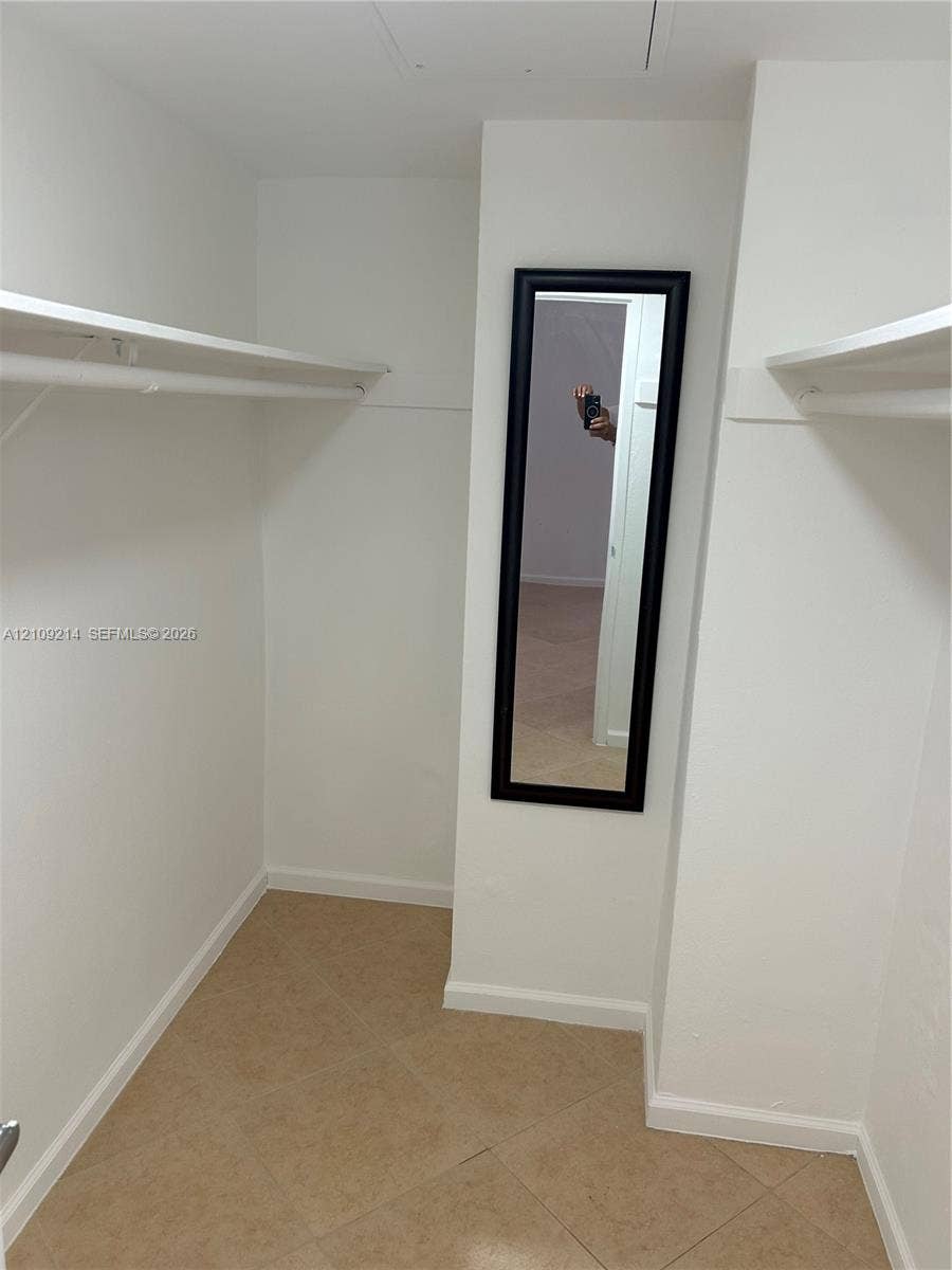 Walk-in storage space featuring ceramic tile flooring, built-in shelving, and a wall-mounted mirror