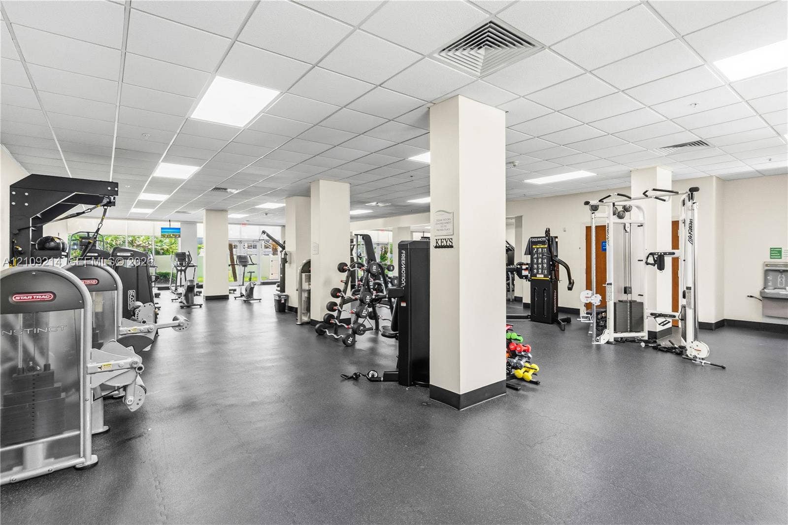 Fitness facility featuring impact-resistant rubber flooring, recessed drop-ceiling grid lighting, and structural support columns