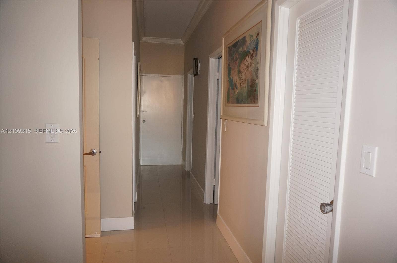 Hallway featuring neutral-toned walls, crown molding, polished tile flooring, and a louvered bi-fold closet door