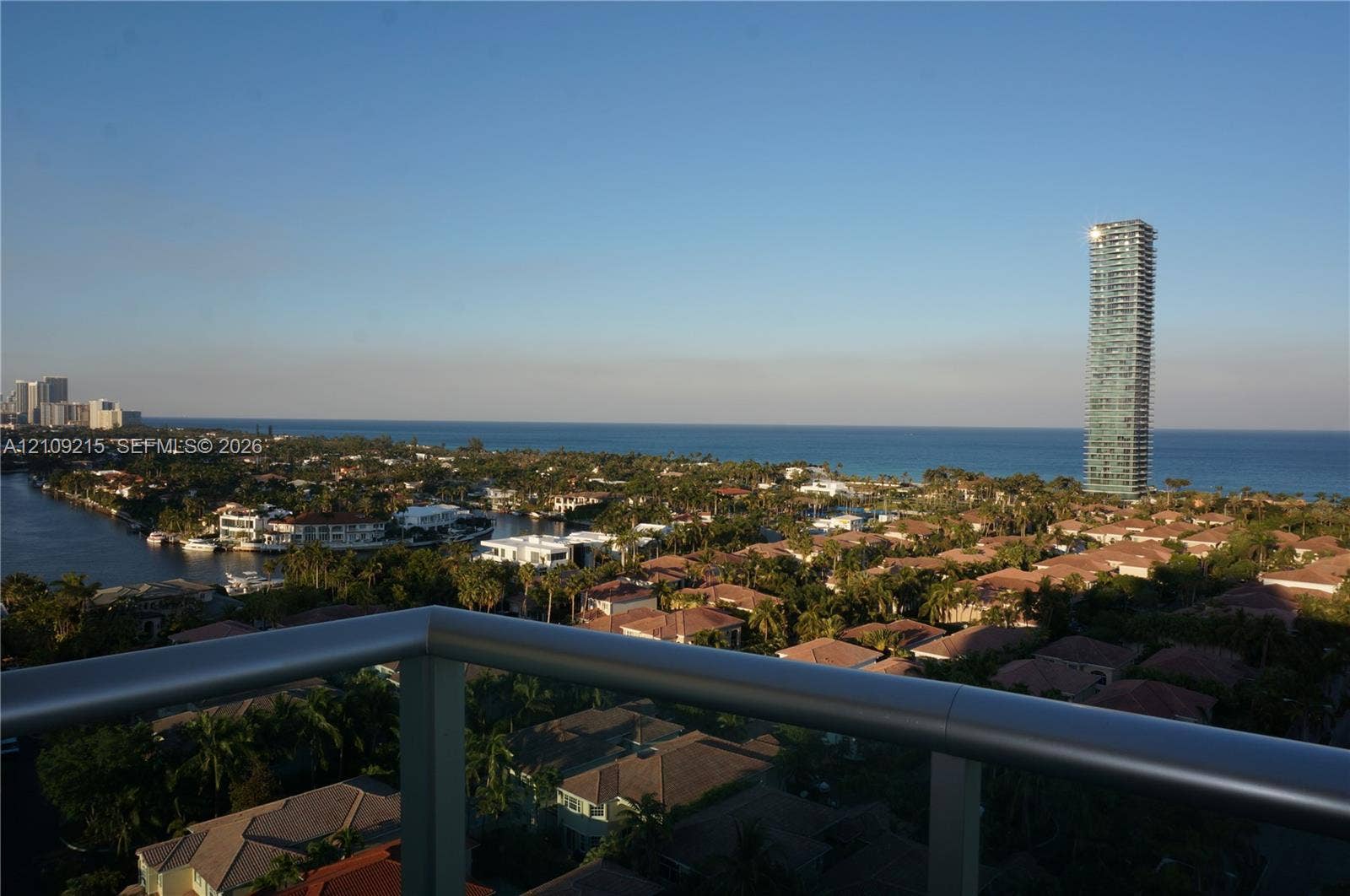 Private balcony with a metal railing, featuring panoramic coastal and cityscape scenery including waterfront areas and high-rise architecture